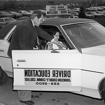 A driver's ed teacher shows a student the inside of a car.